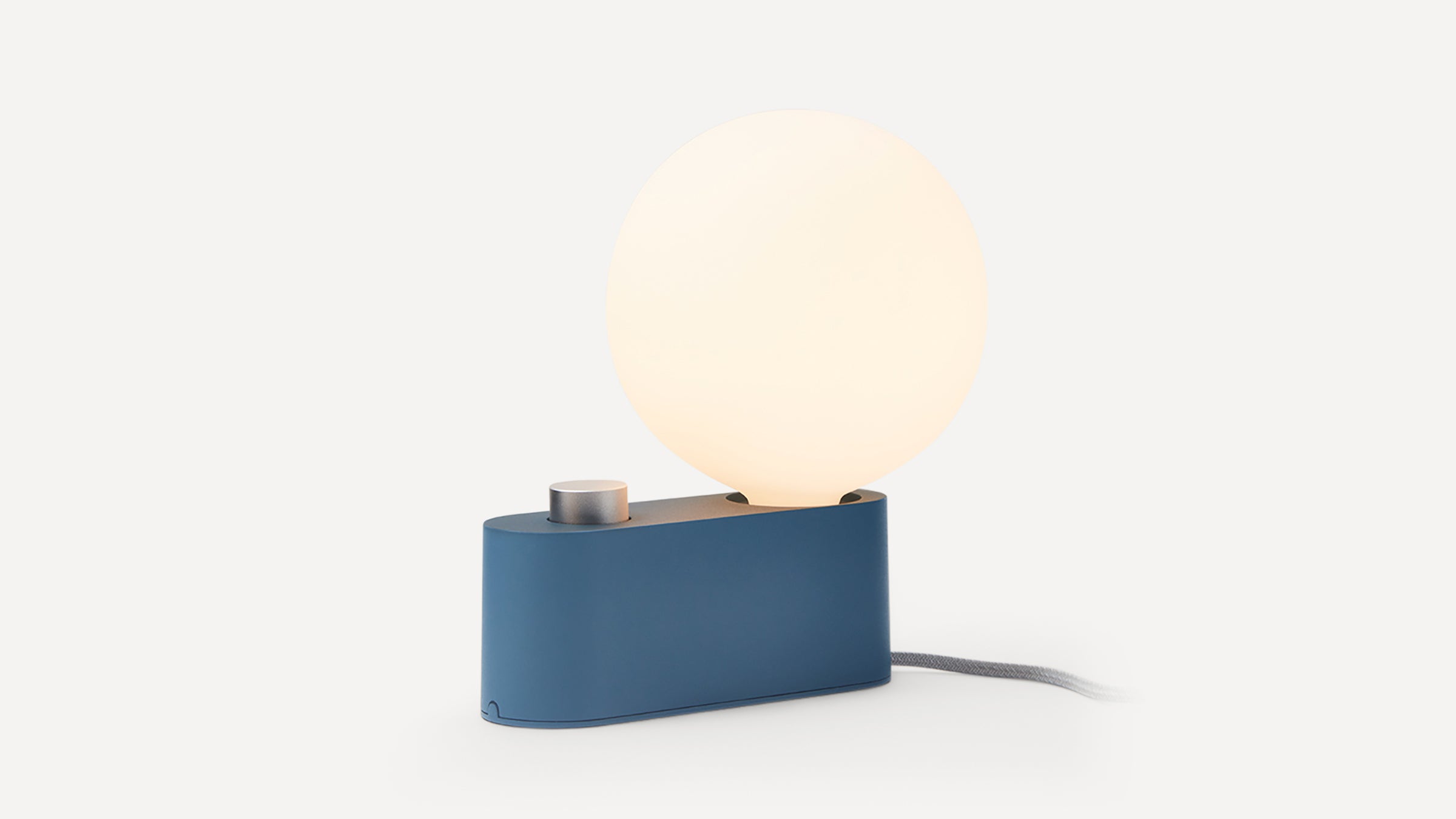 Modern table lamp with a large round frosted glass bulb and a matte blue rectangular base with a silver knob.