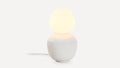 Modern table lamp with a rounded white ceramic base and a soft glowing frosted glass shade, emitting warm light.