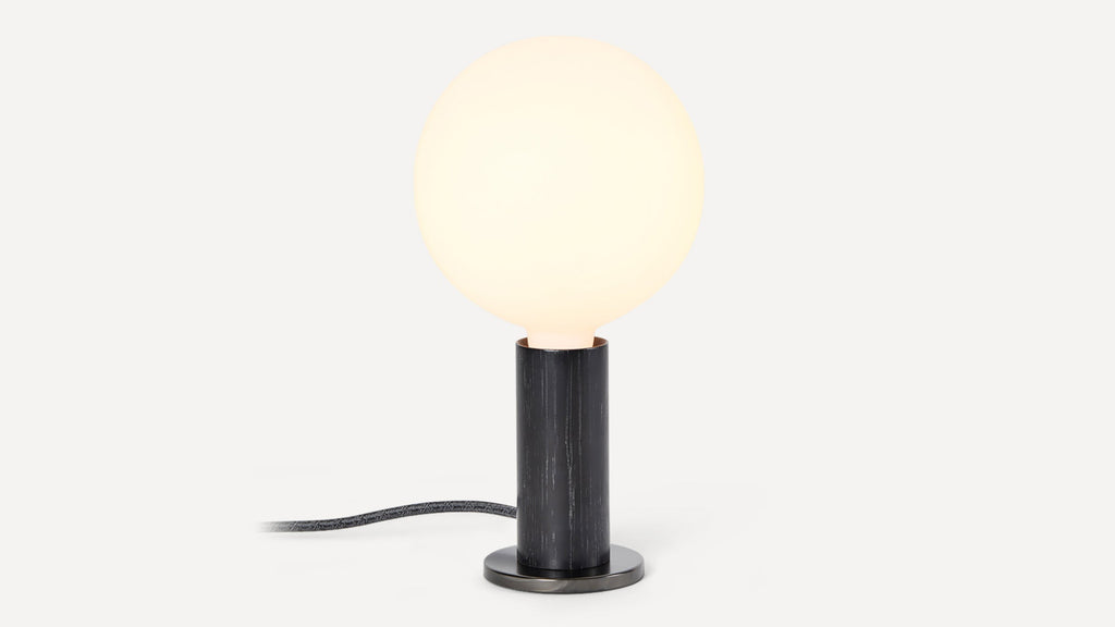 Small modern table lamp with a glowing round white glass bulb on a cylindrical black wooden base.