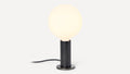 Small modern table lamp with a glowing round white glass bulb on a cylindrical black wooden base.