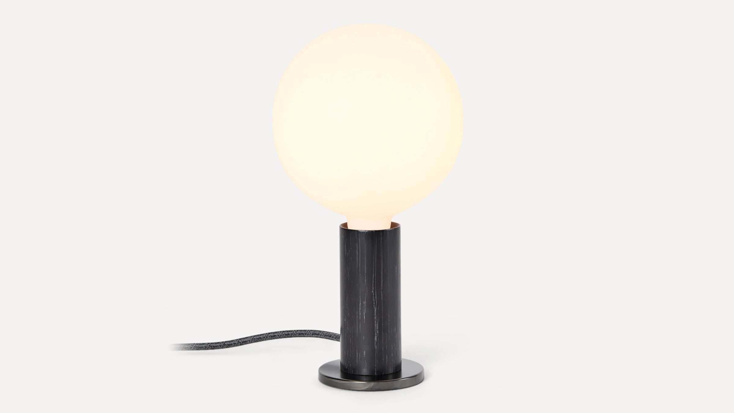 Small modern table lamp with a glowing round white glass bulb on a cylindrical black wooden base.