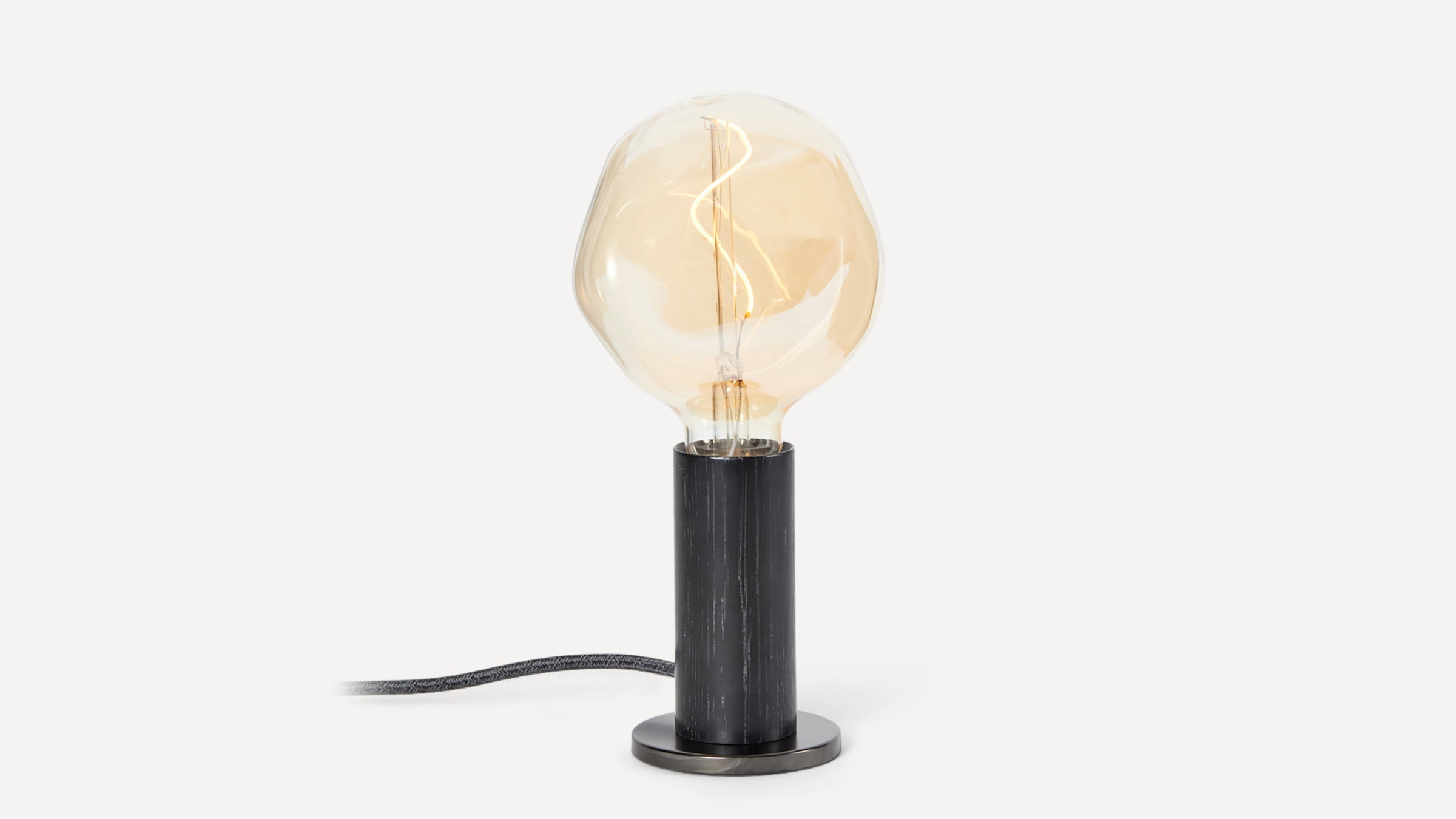 Modern table lamp with a large round amber filament bulb and black cylindrical base on a white background.