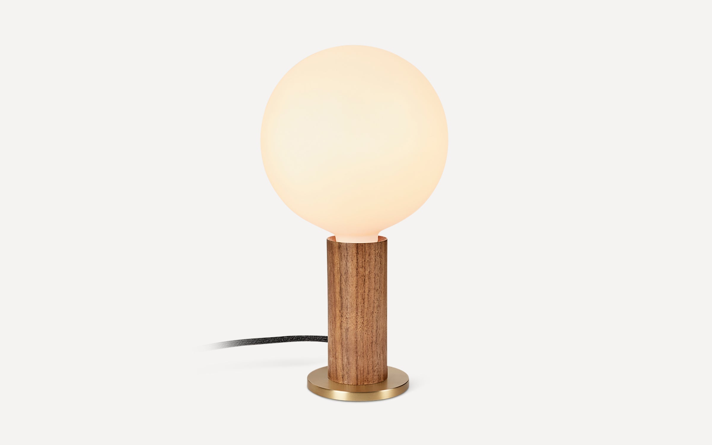Table lamp with a round frosted glass shade, wooden cylindrical base, and brass circular bottom, connected by a black cord.