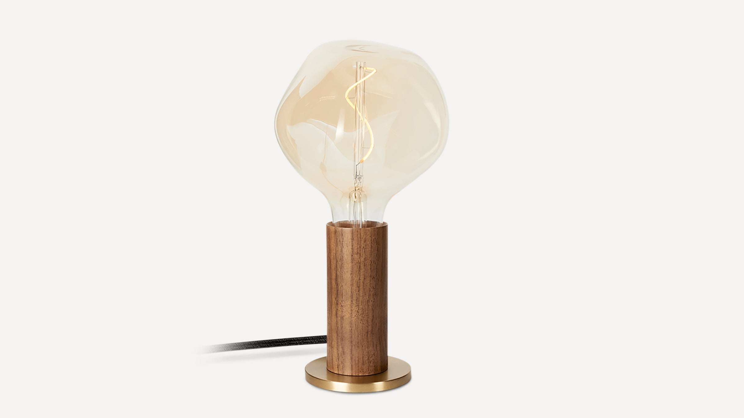 Table lamp with a clear, irregularly shaped glass bulb, wooden cylindrical base, and round brass-colored metal stand.