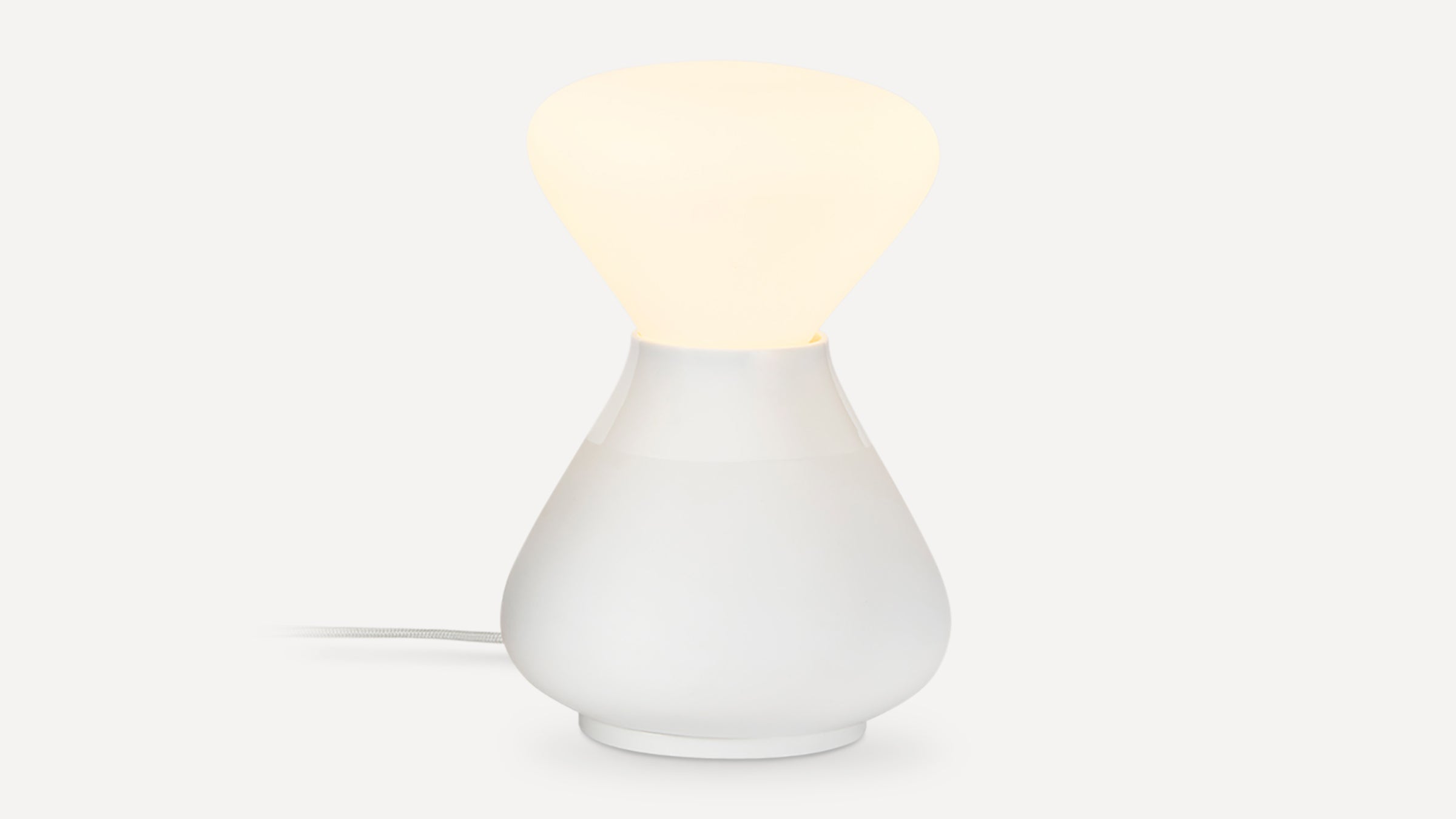 White modern table lamp with a rounded base and soft glowing top, connected by a fabric-covered cord.
