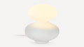 Modern white table lamp with rounded base and oval frosted glass shade emitting soft warm light.