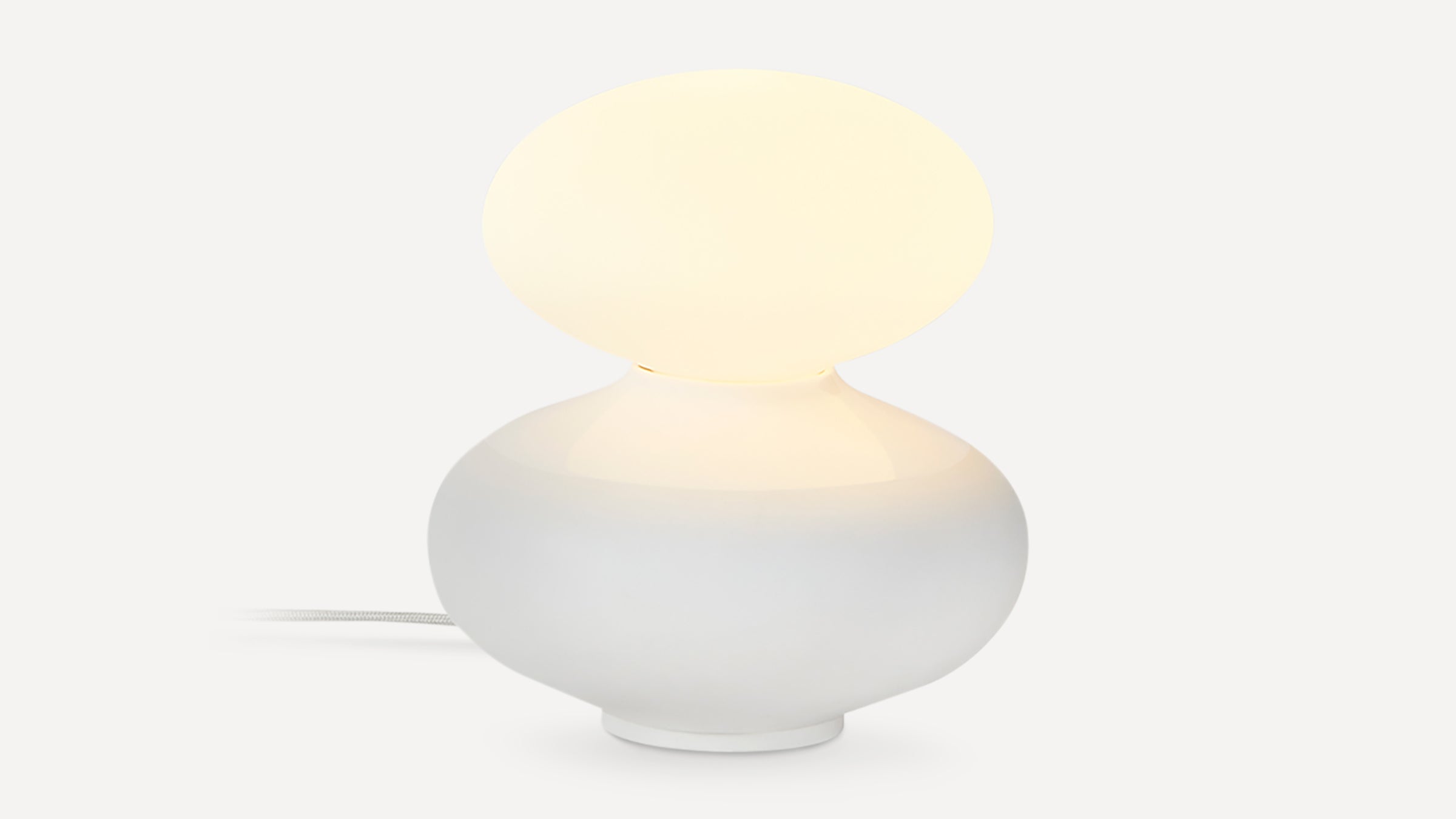 Modern white table lamp with rounded base and oval frosted glass shade emitting soft warm light.