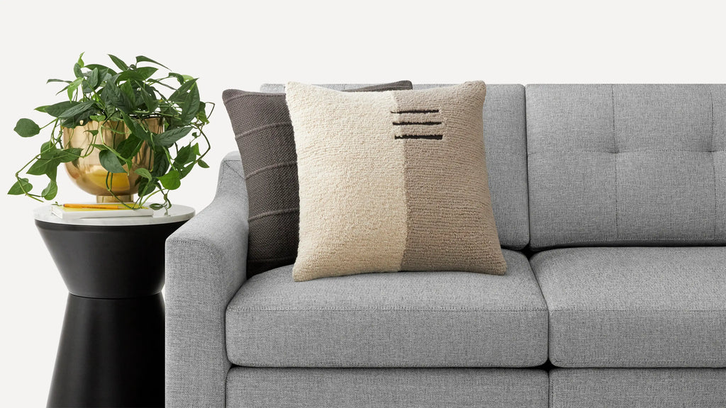 a gray couch with a pillow and a plant on the side table