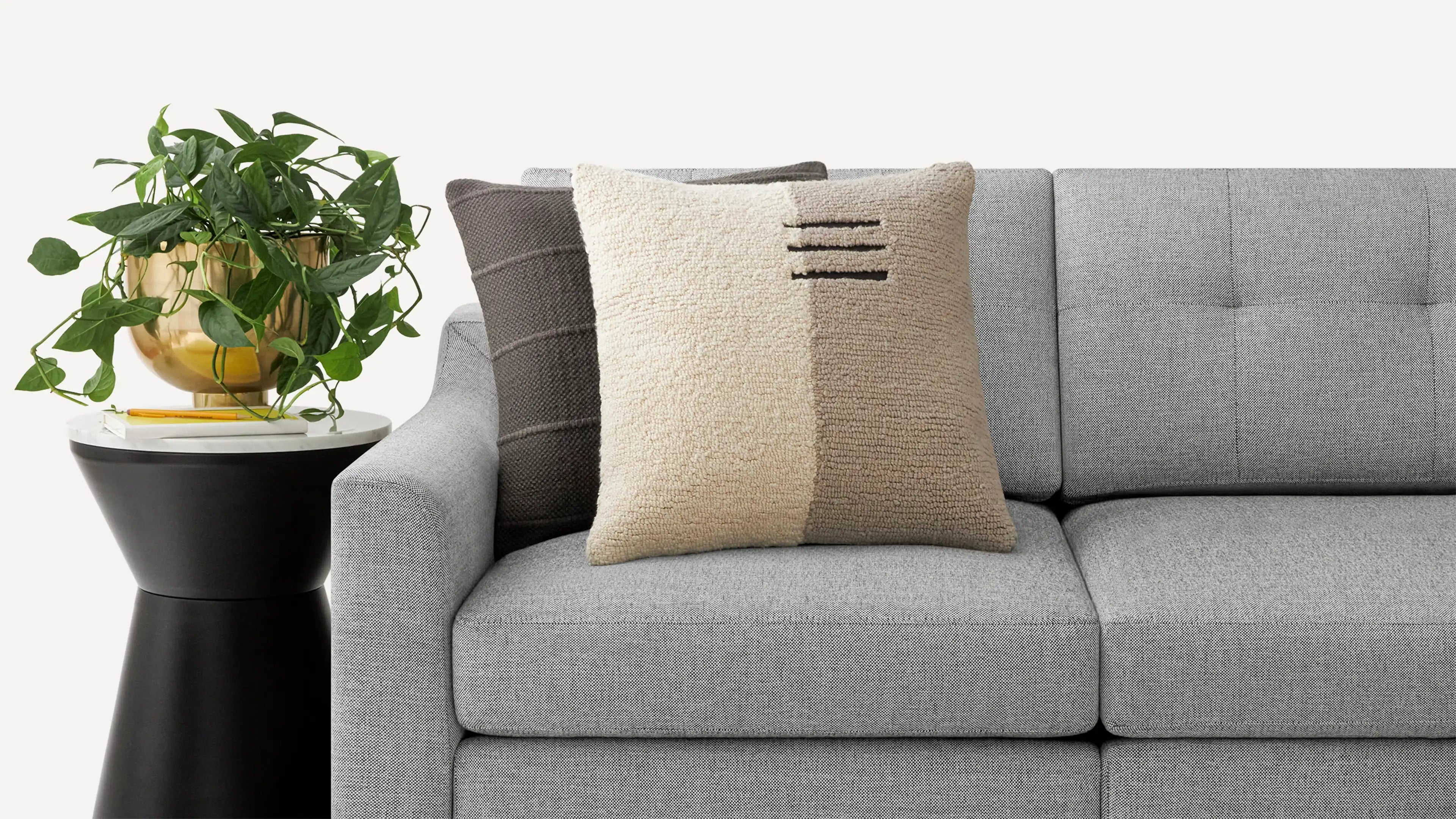a gray couch with a pillow and a plant on the side table