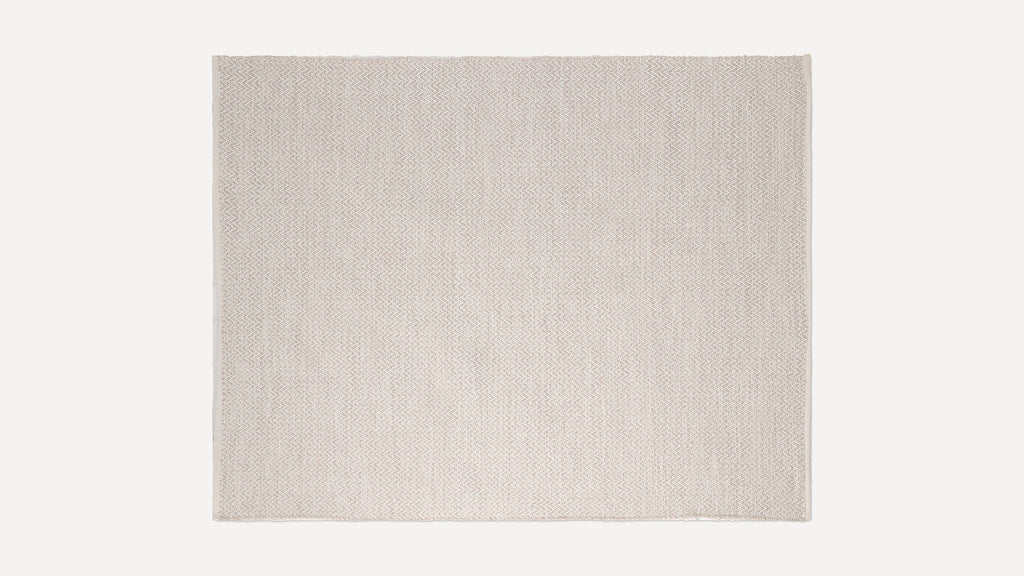 Beige woven rectangular rug with subtle chevron pattern and fringed edges, displayed on a plain white background.