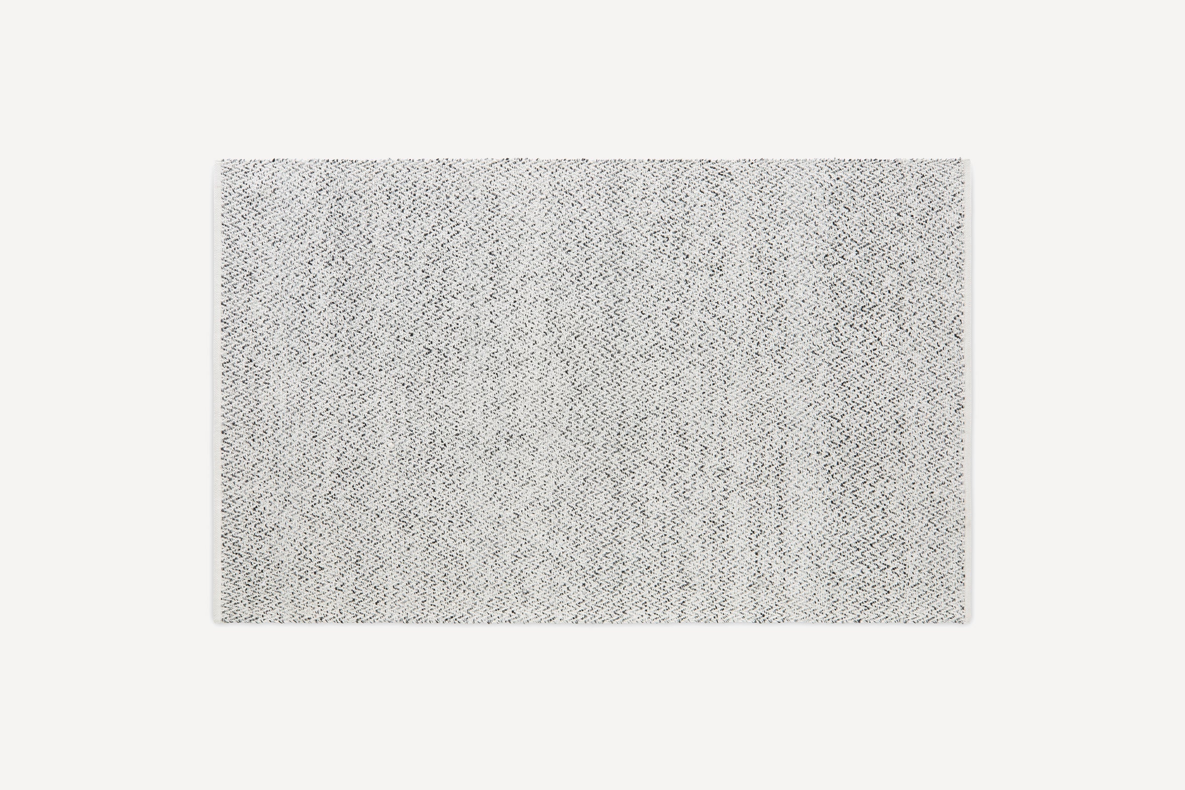 Rectangular rug with a subtle, light gray and white herringbone pattern, featuring neatly finished edges on a plain background.