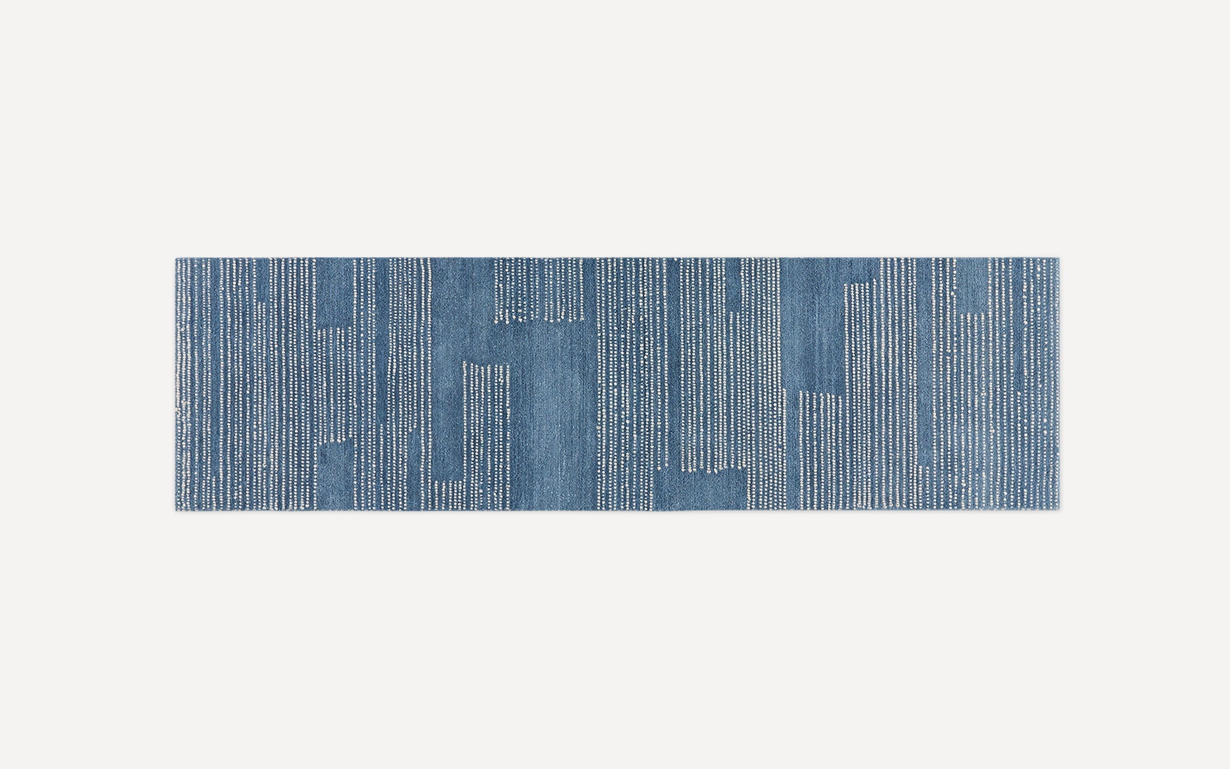 Blue rectangular runner rug with vertical white dotted stripes and irregular block patterns on a light background.