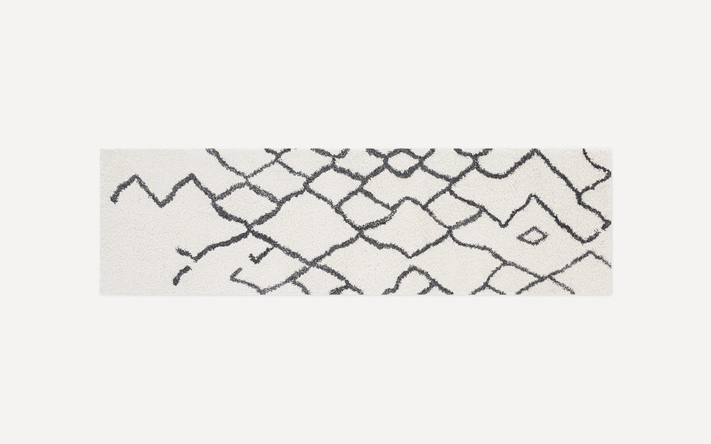 Long rectangular white rug with a black abstract geometric diamond pattern and a soft, plush texture.