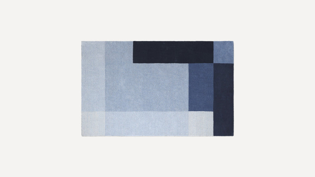 Rectangular rug with a geometric pattern in various shades of blue, including light, medium, and dark tones.