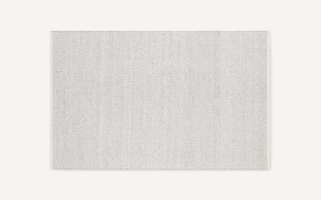 Rectangular light gray area rug with subtle small-scale woven chevron pattern, simple and modern design, flat weave texture.