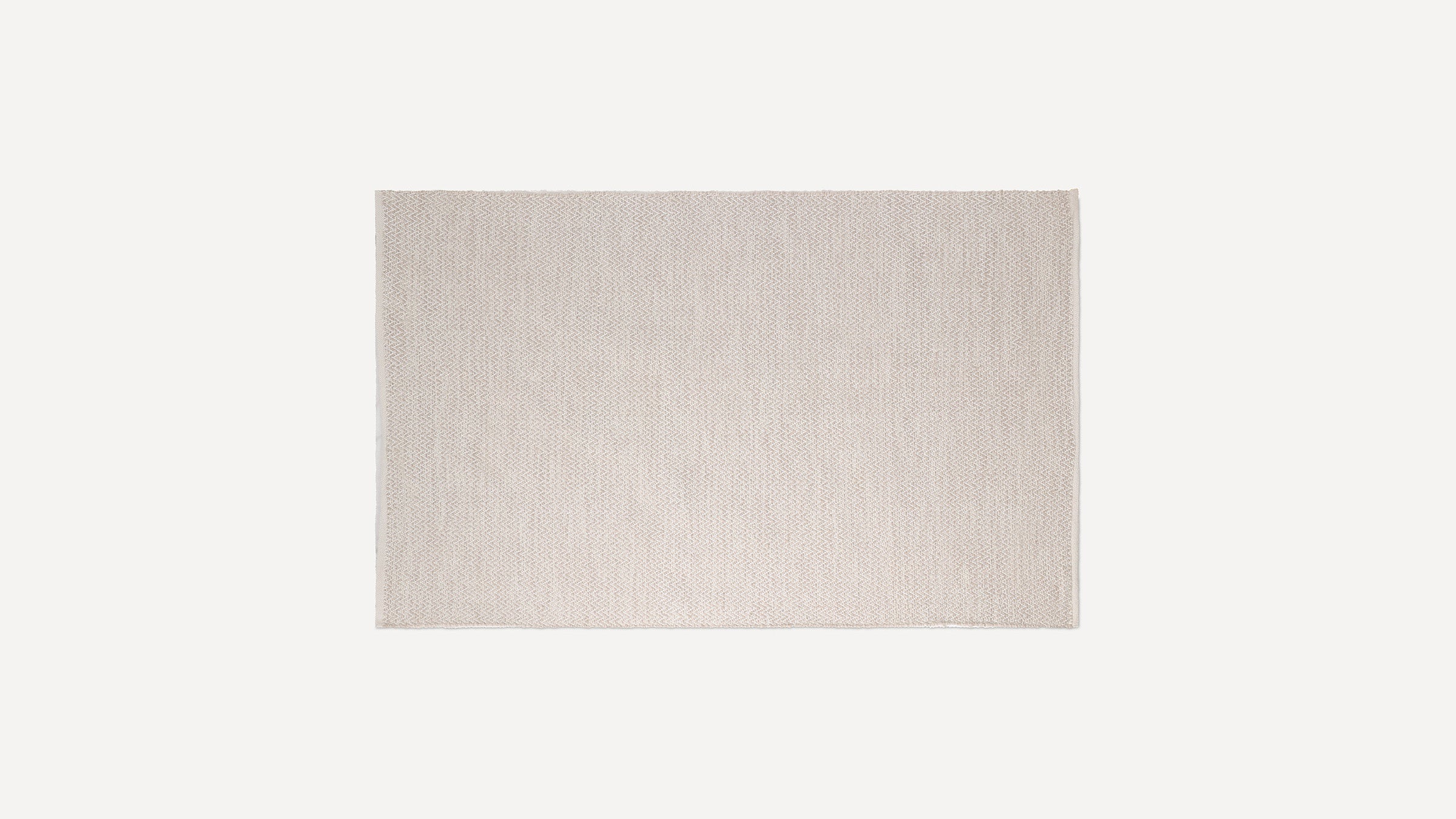 Rectangular beige woven rug with subtle herringbone pattern and fringe edges, displayed flat on white background.