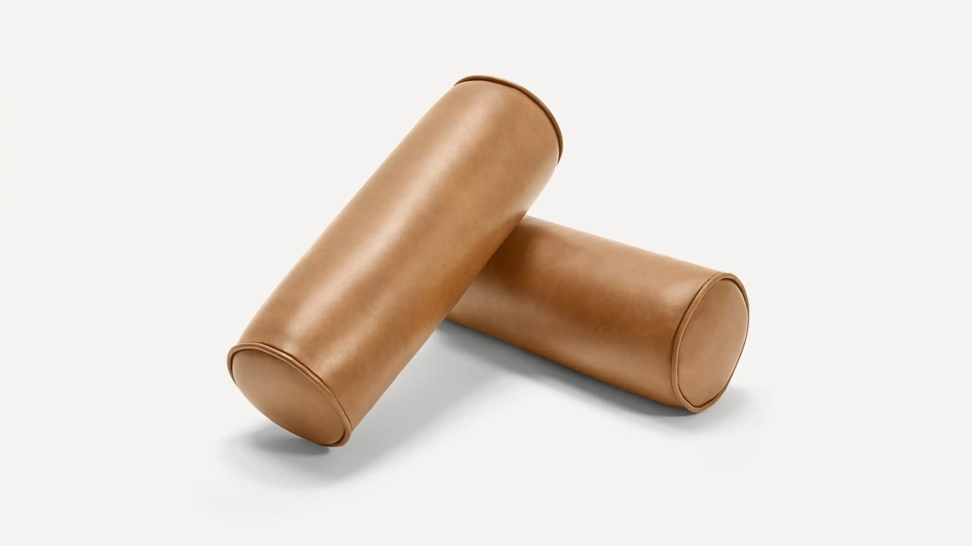 Two cylindrical brown leather bolster pillows arranged on a light background, showing smooth texture and stitched edges.