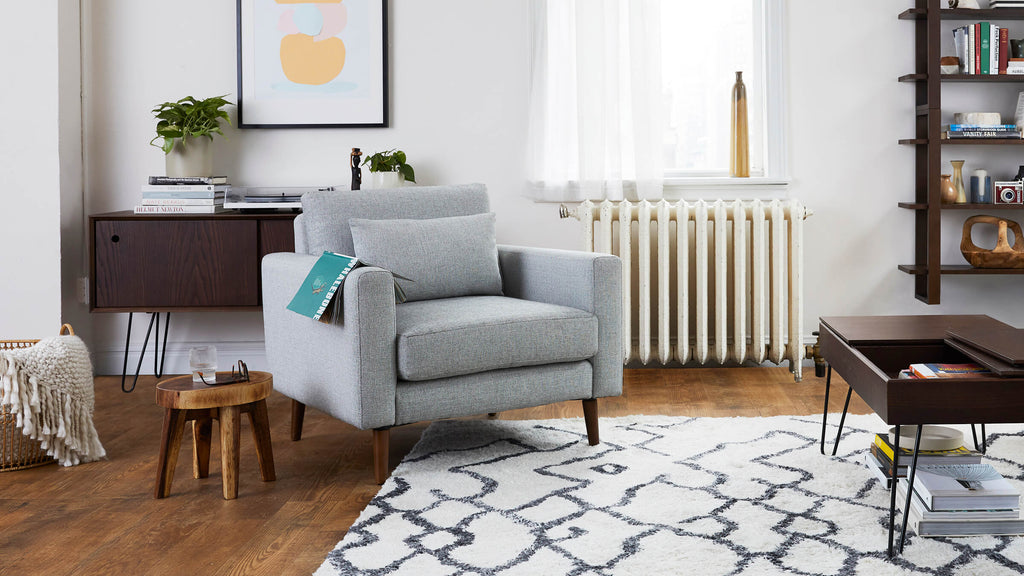 a living room with a gray armchair, a wooden coffee table, and a white rug
