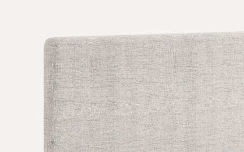 Close-up of a light gray textured fabric headboard with clean, rounded edges and a modern minimalist design.