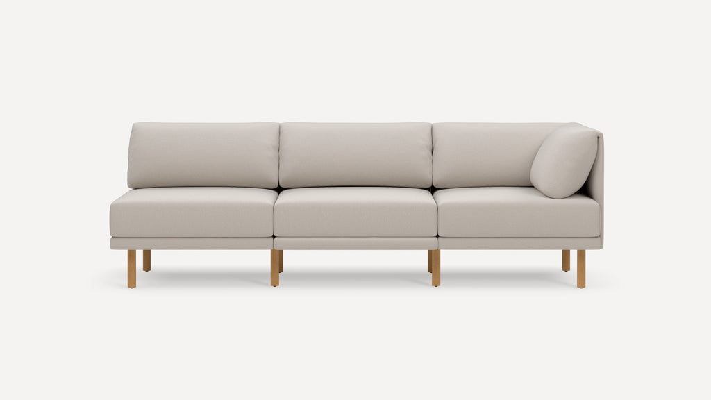 Modern light beige three-seater sofa with wooden legs, clean lines, and a small cylindrical pillow on the right side.