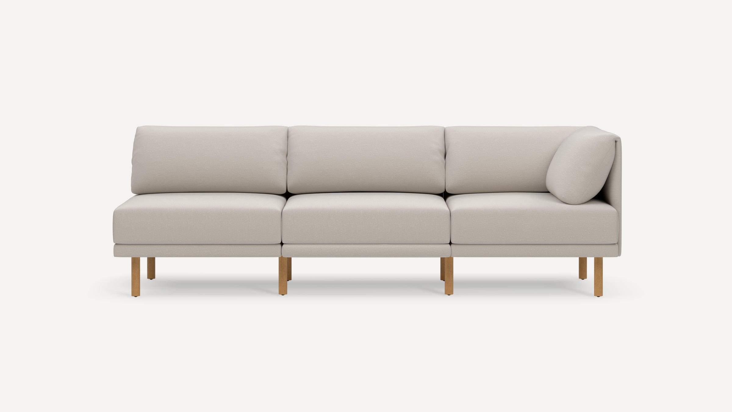 Modern light beige three-seater sofa with wooden legs, clean lines, and a small cylindrical pillow on the right side.