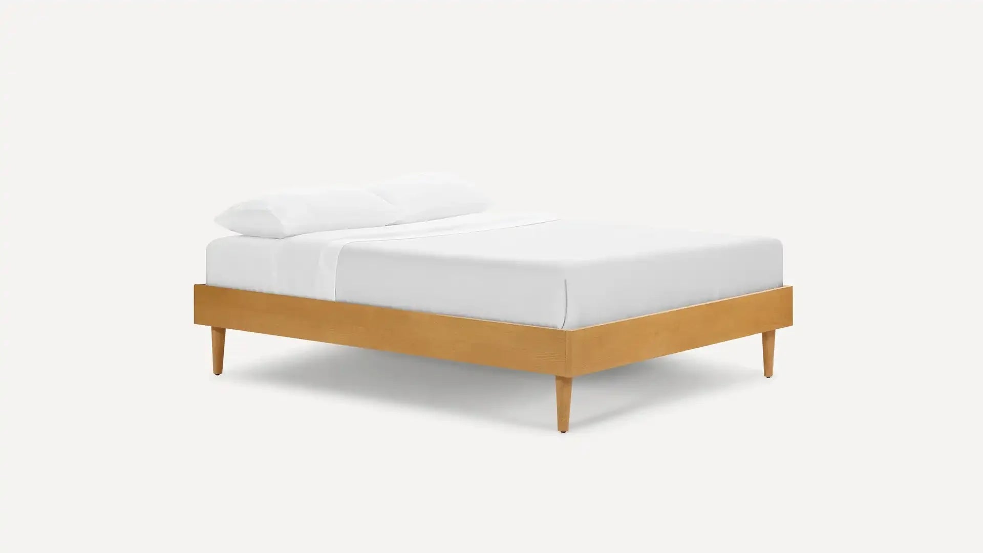 Minimalist wooden bed frame with tapered legs, dressed in white bedding and two pillows, displayed on a plain background.