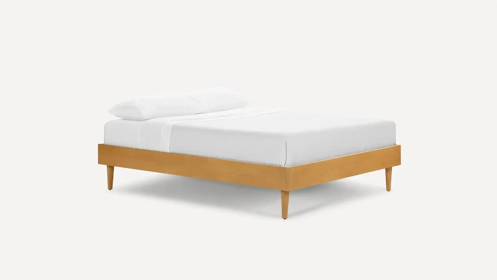 Modern wooden bed frame with tapered legs, dressed in white bedding and pillows, shown against a plain background.