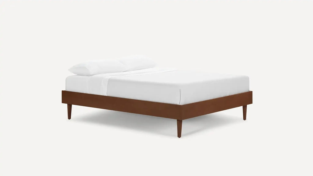 Mid-century modern wooden bed frame with tapered legs, fitted with white bedding and two pillows.