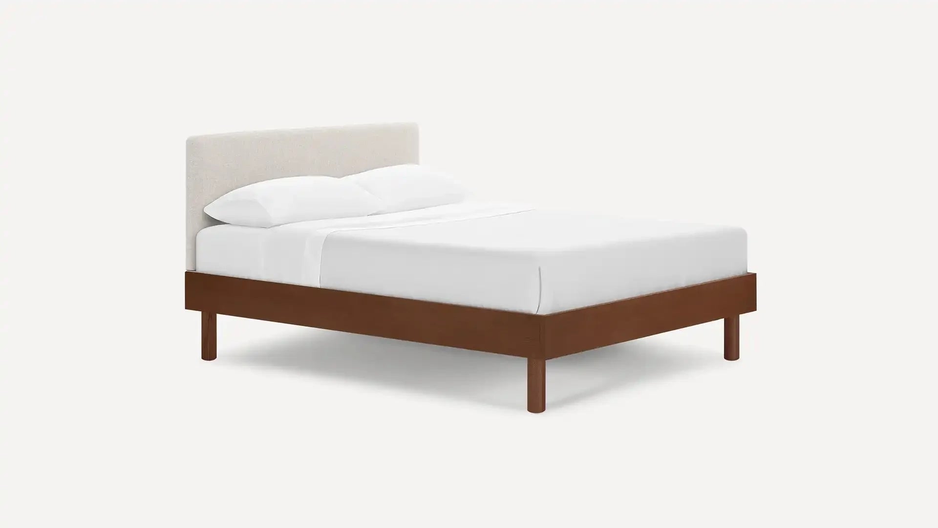 Modern bed frame with walnut wooden legs and base, beige upholstered headboard, and neatly made white bedding with pillows.