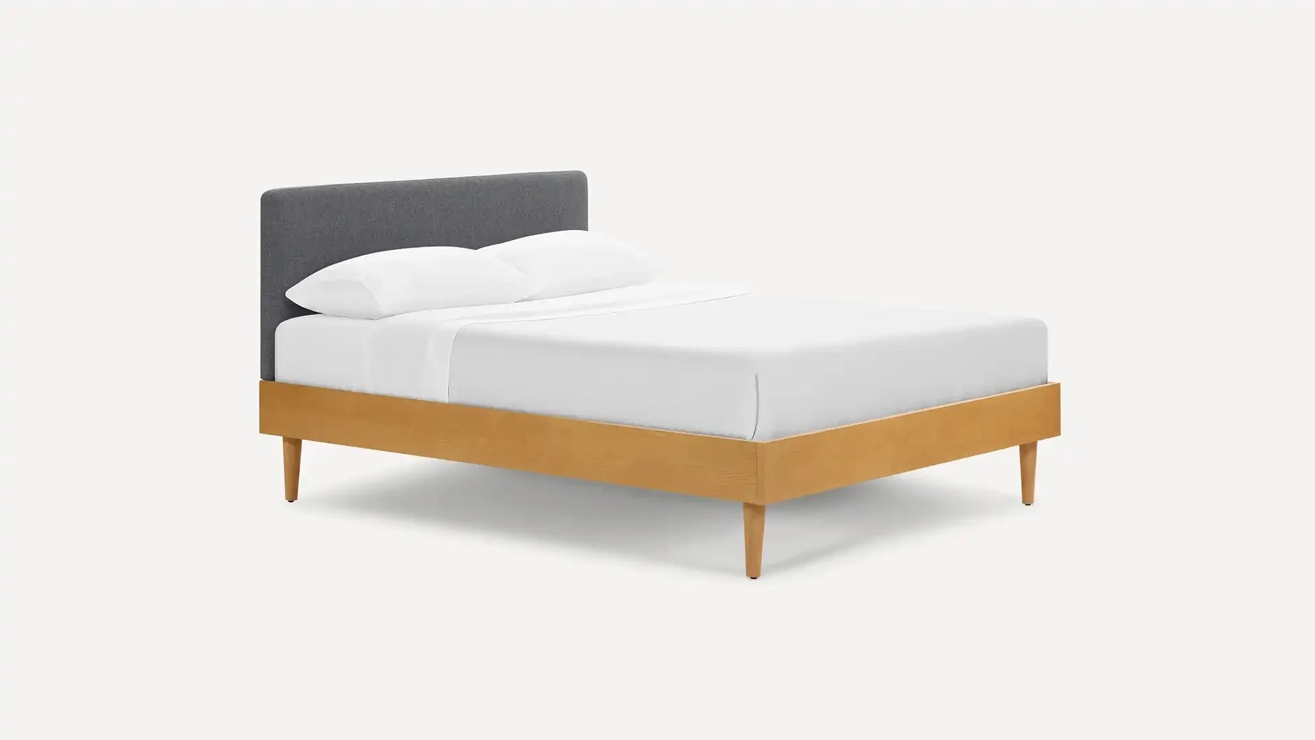Modern platform bed with light wood frame, tapered legs, and dark gray upholstered headboard, dressed in white bedding.