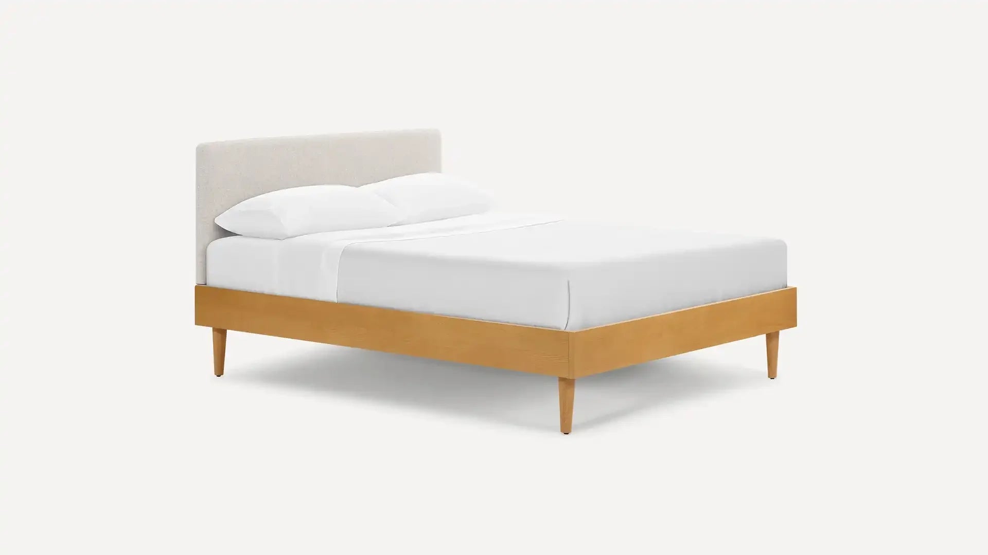 Mid-century modern platform bed with light wood frame, angled legs, and upholstered beige fabric headboard, dressed in white bedding.
