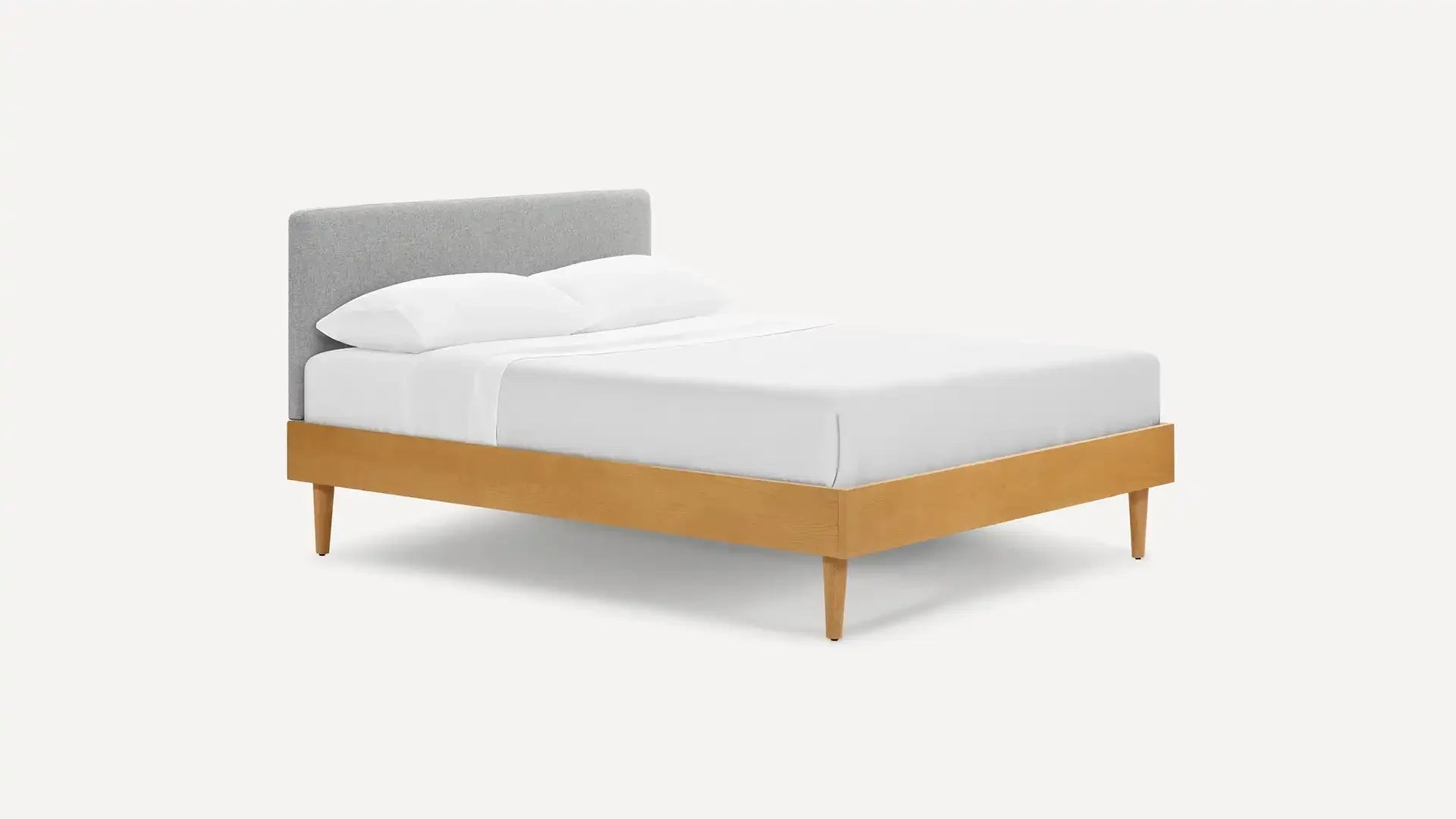 Modern bed with light wood frame and tapered legs, featuring a soft gray upholstered headboard and white bedding.