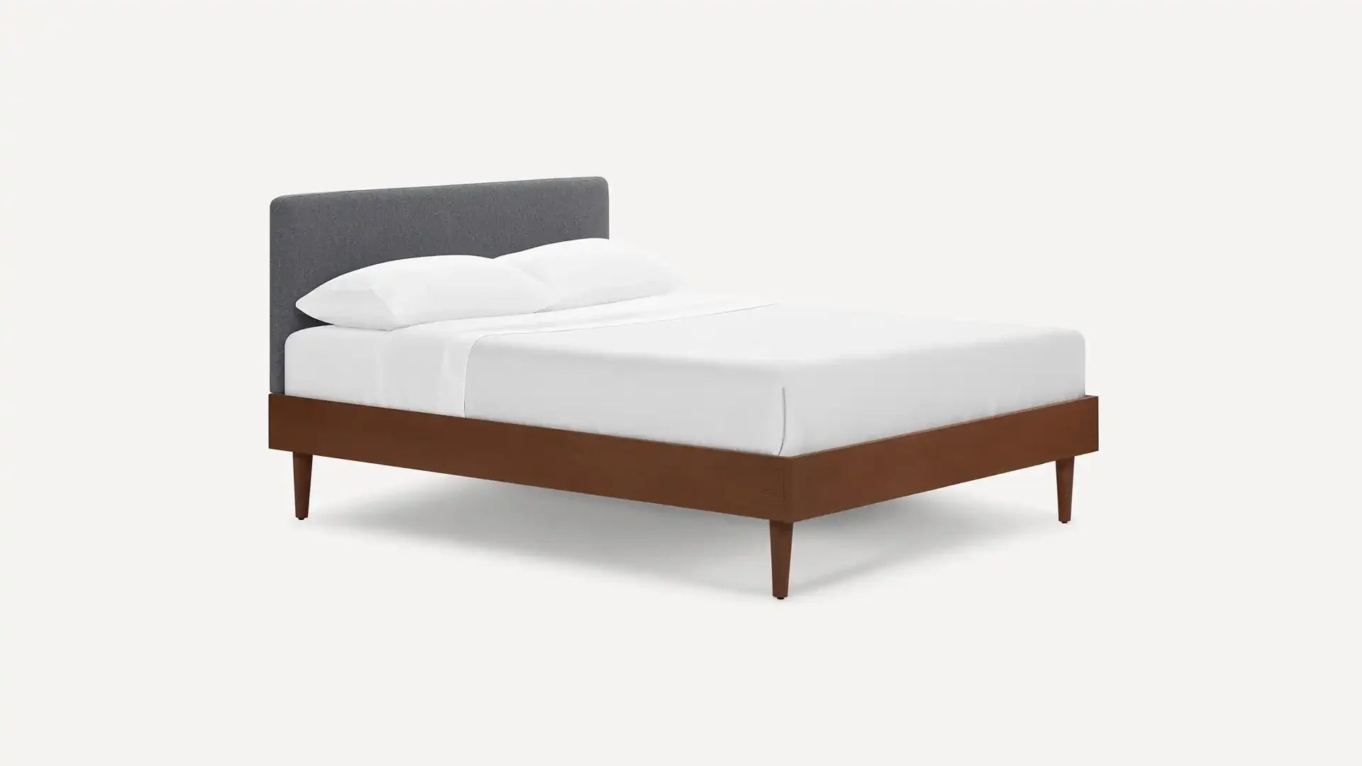 Modern bed with a dark grey upholstered headboard, white bedding, and a wooden frame with tapered legs.