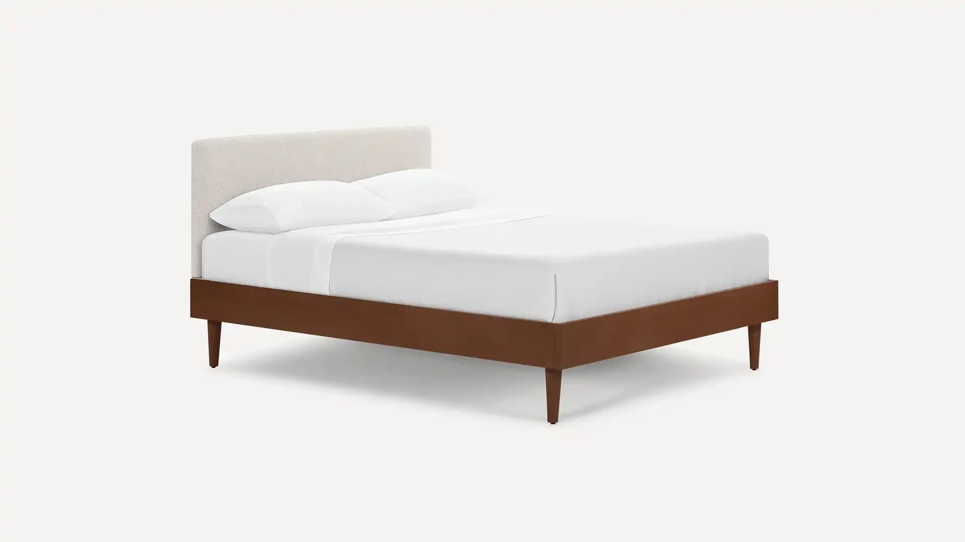 Modern platform bed with a wooden frame, tapered legs, and an upholstered beige headboard, dressed with white bedding.