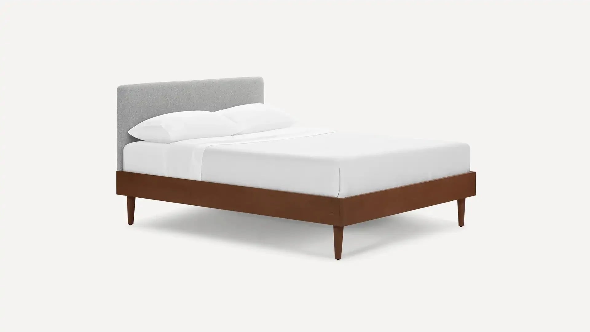 Modern wooden platform bed with tapered legs and a light gray upholstered headboard, dressed in white bedding.
