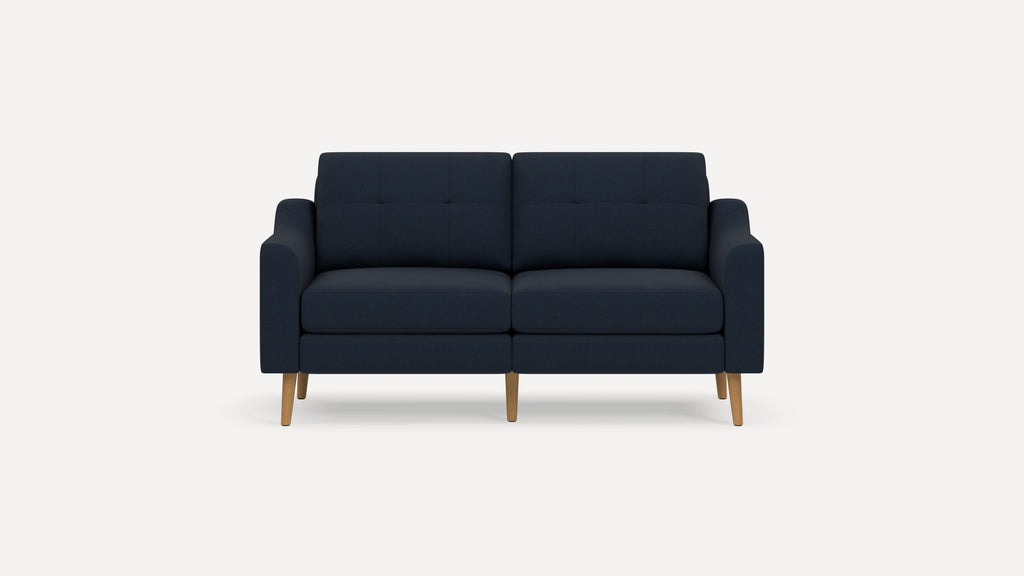 Modern navy blue two-seater sofa with tufted cushions, straight armrests, and light wooden legs on white background.