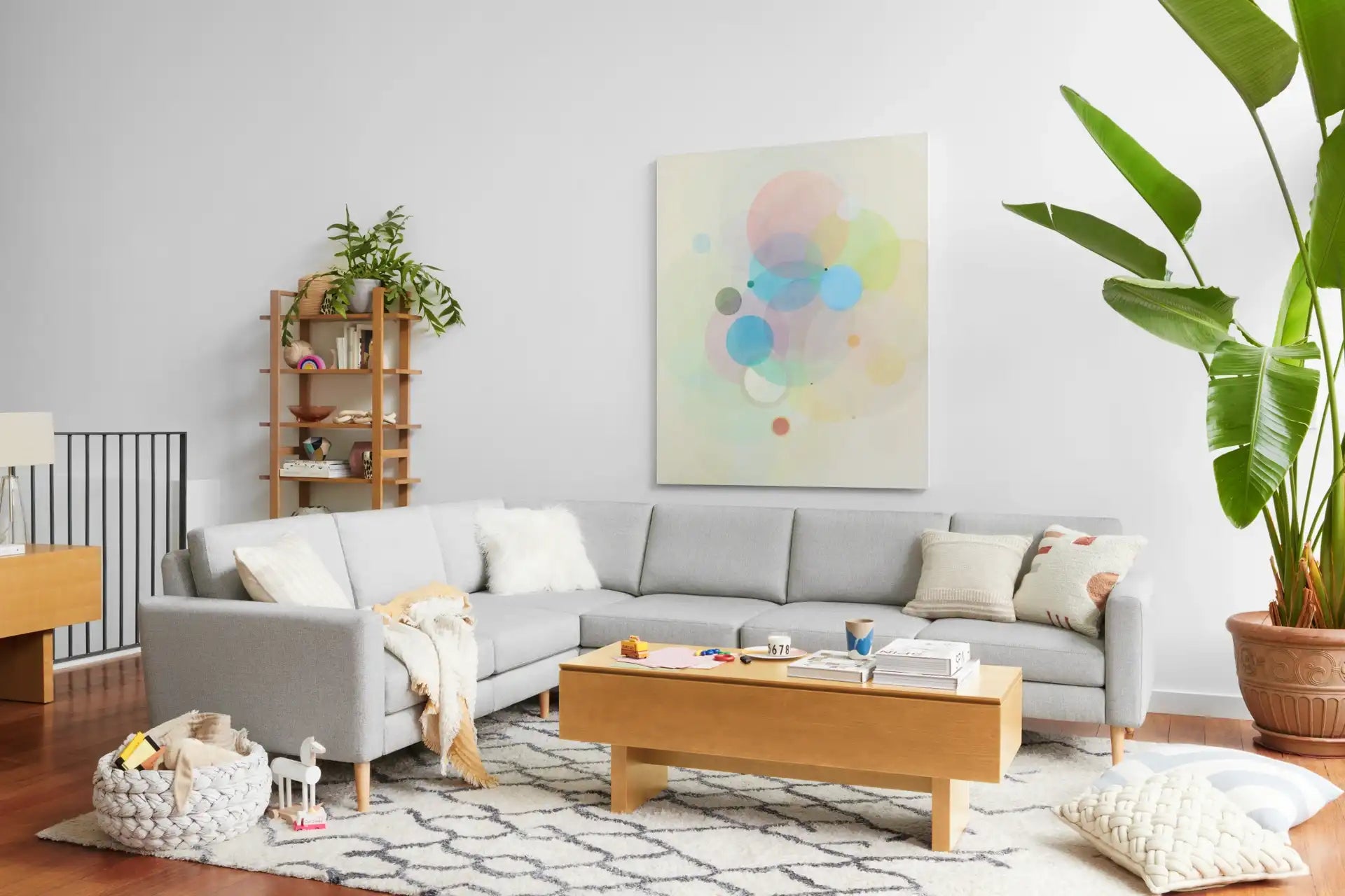 modern living room with light gray sectional sofa, light gray rug, wooden coffee table, and monster plant on wall