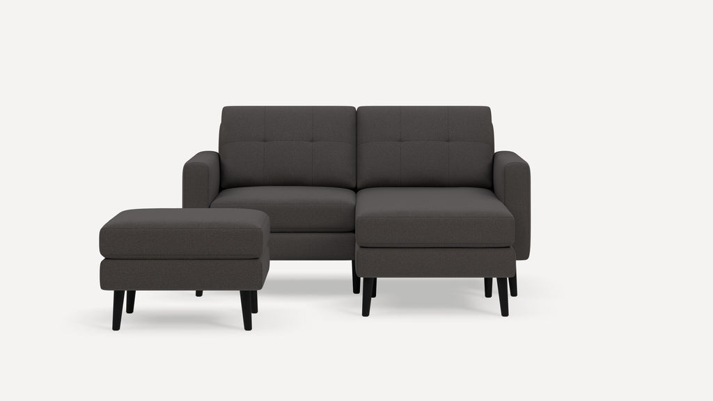 Modern dark gray upholstered sectional sofa with separate matching ottoman and black wooden legs on white background.