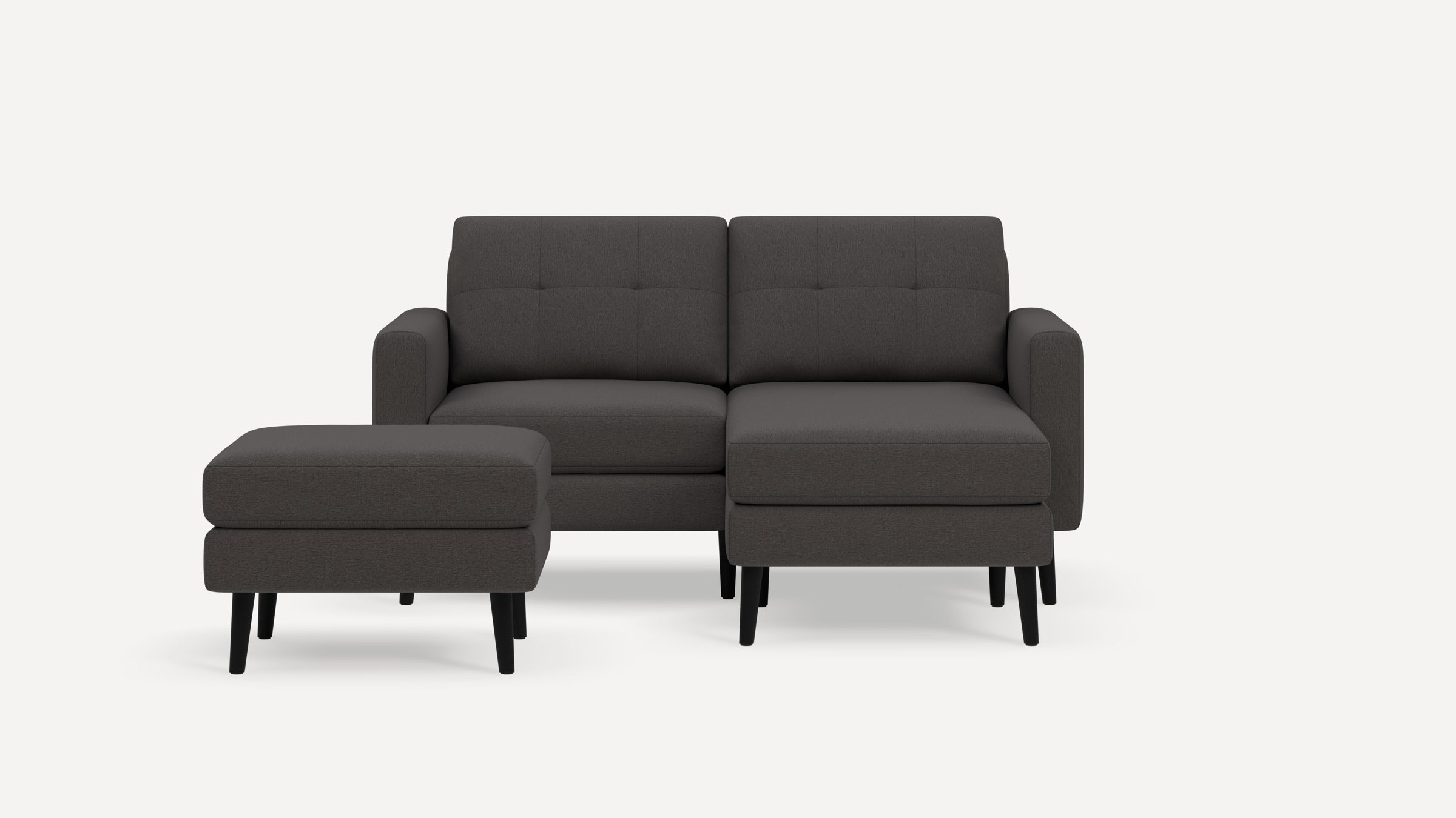 Modern dark gray upholstered sectional sofa with separate matching ottoman and black wooden legs on white background.