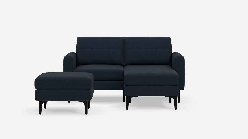 Modern navy blue fabric sectional sofa with matching ottoman, tufted cushions, and black slender legs on a white background.