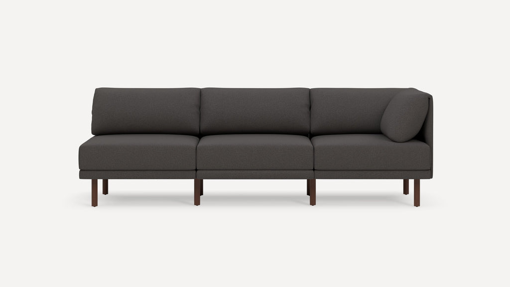 Modern dark gray three-seater sofa with wooden legs and a single cylindrical cushion on the right side.
