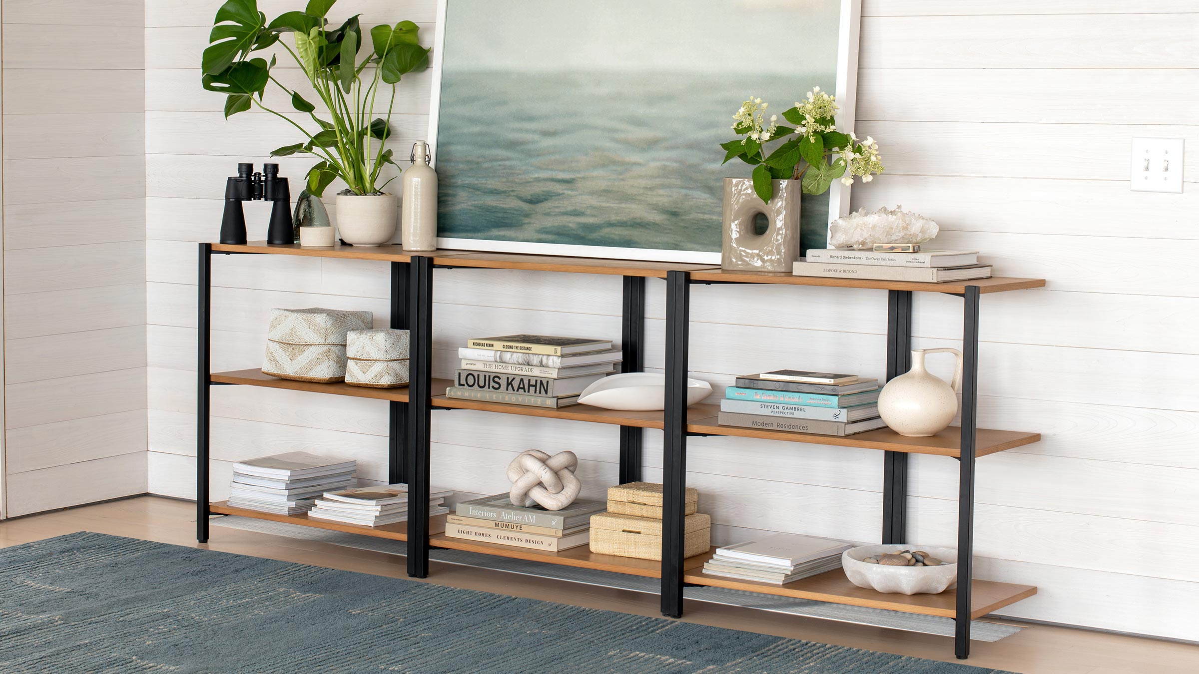 a living room with a large picture on the wall and a shelf with books, vases, and plants on it