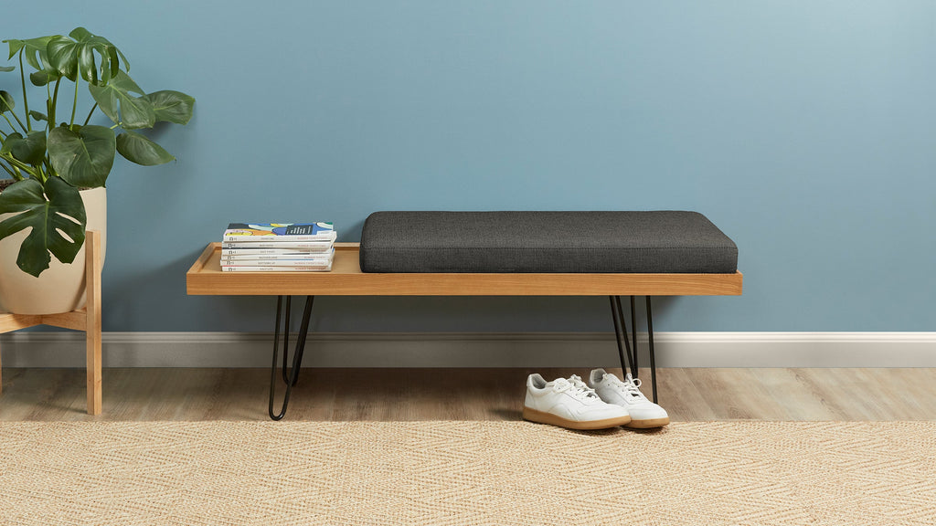 a wooden bench with a black cushion and a plant on top of it