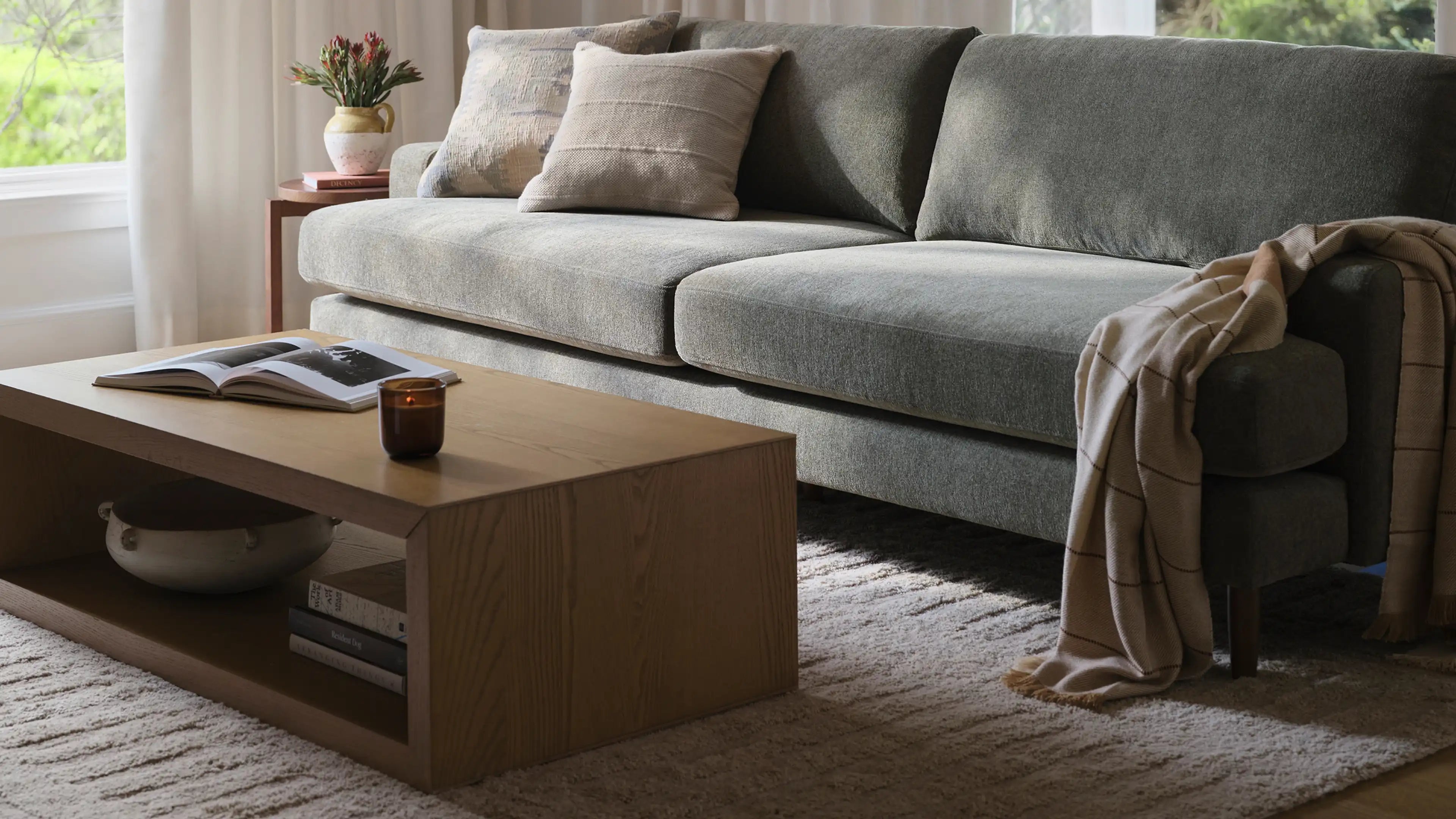 Modern gray upholstered sofa with matching cushions, beige throw, wooden coffee table, and decorative accents in a cozy living room.