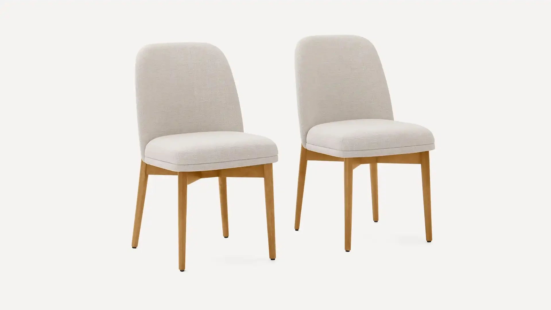 Two modern dining chairs with beige upholstered seats and backs, supported by light wooden legs, on a plain background.