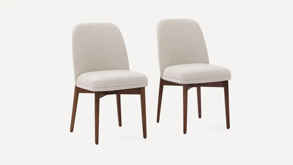 Two beige upholstered dining chairs with rounded backs and walnut-finished wooden legs on a white background.