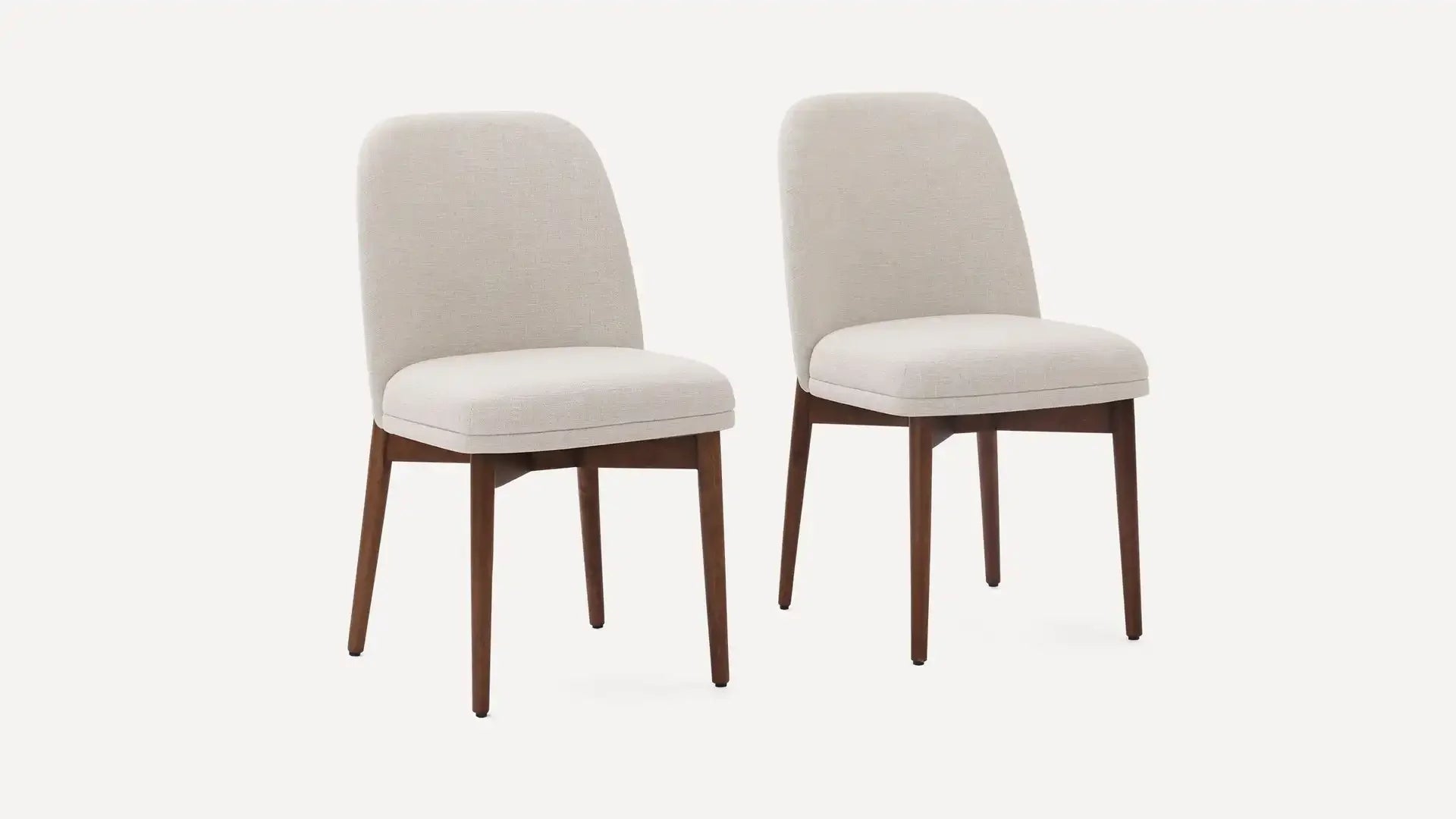 Two beige upholstered dining chairs with rounded backs and walnut-finished wooden legs on a white background.