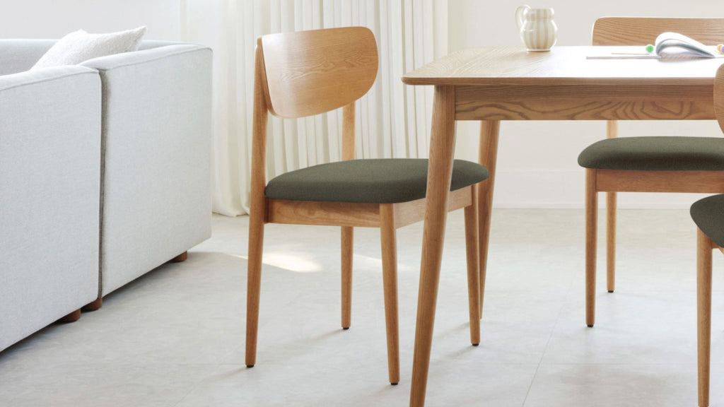 Wooden dining chair with dark cushioned seat, paired with a matching wooden table in a bright, modern room.