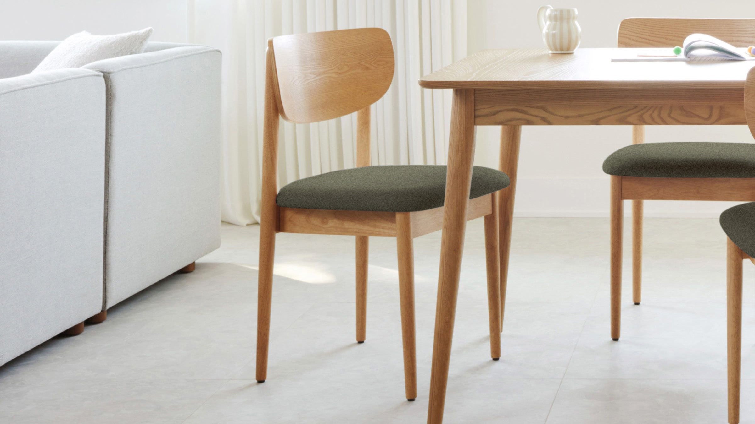 Wooden dining chair with dark cushioned seat, paired with a matching wooden table in a bright, modern room.