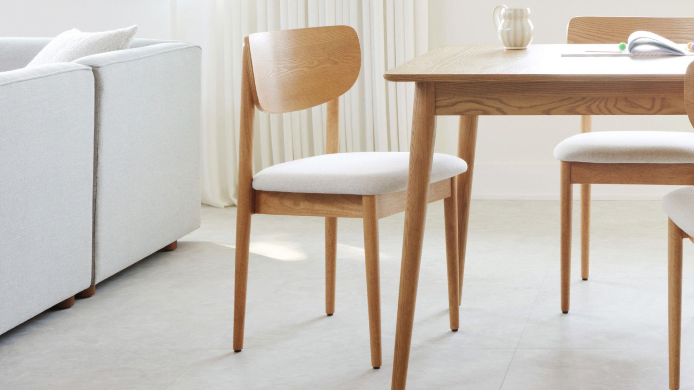 Light wood dining chair with a curved backrest and cushioned white seat, positioned next to a matching wooden table.